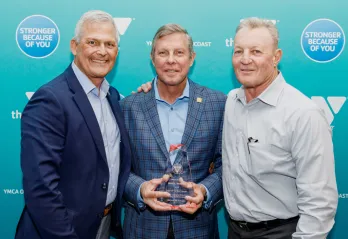 Three men on step and repeat at 2022 Annual Celebration. Man in the middle is holding a glass Order of the Red Triangle award.