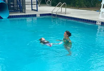 Swim Instructor teaching a young student how to float in the water.