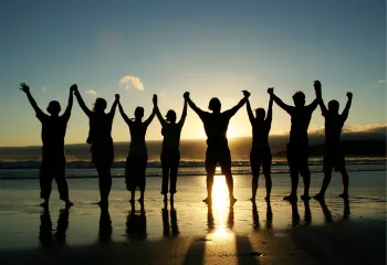 A group of people holding hands on beach as they face the sunset