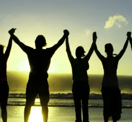 silhouette of people holding raised hands on beach at sunrise