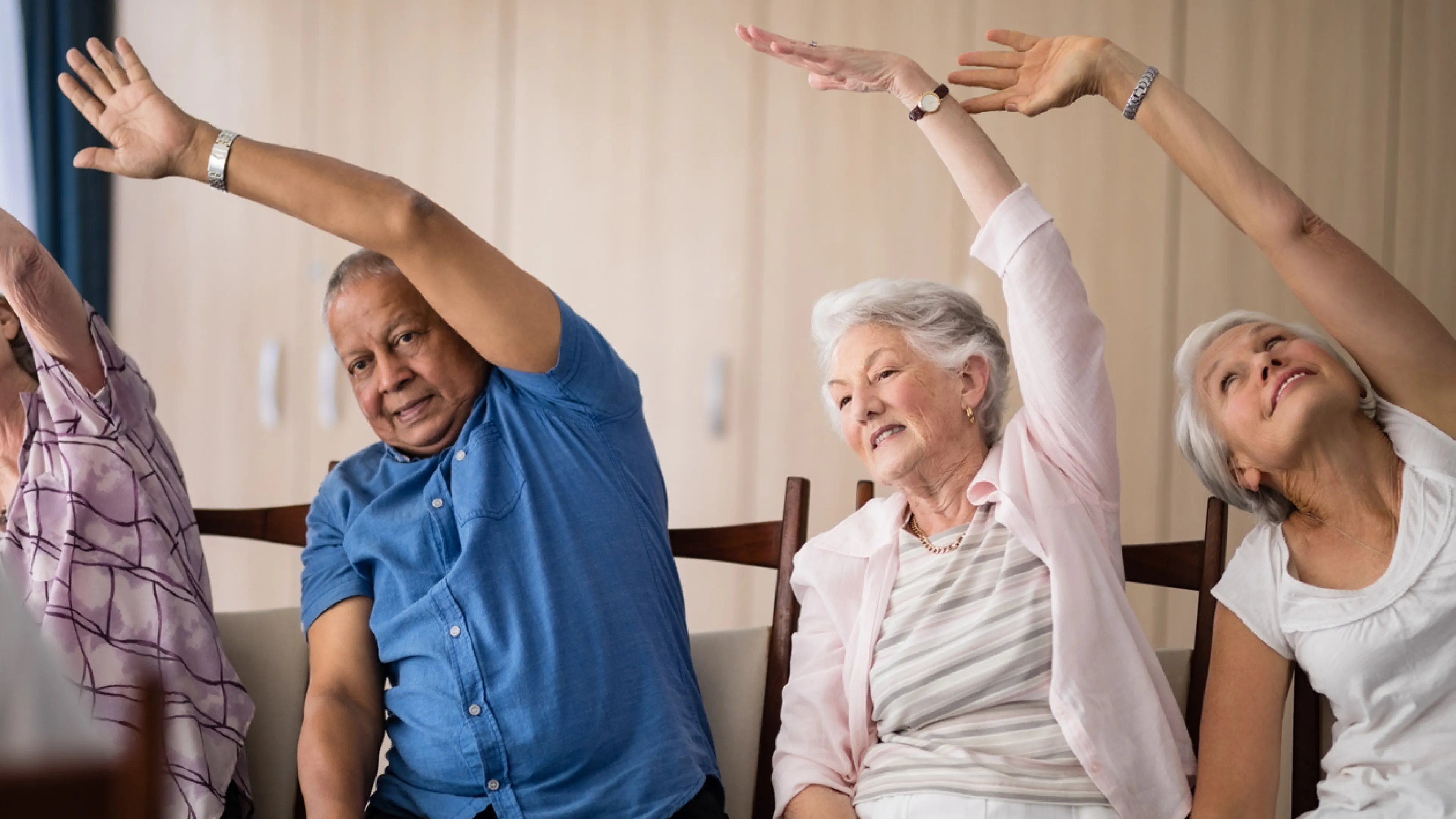 A group of four seniors sitting and reaching one arm to the opposite side.