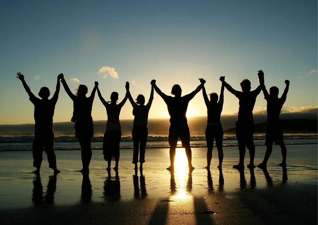A group of people holding hands on beach as they face the sunset