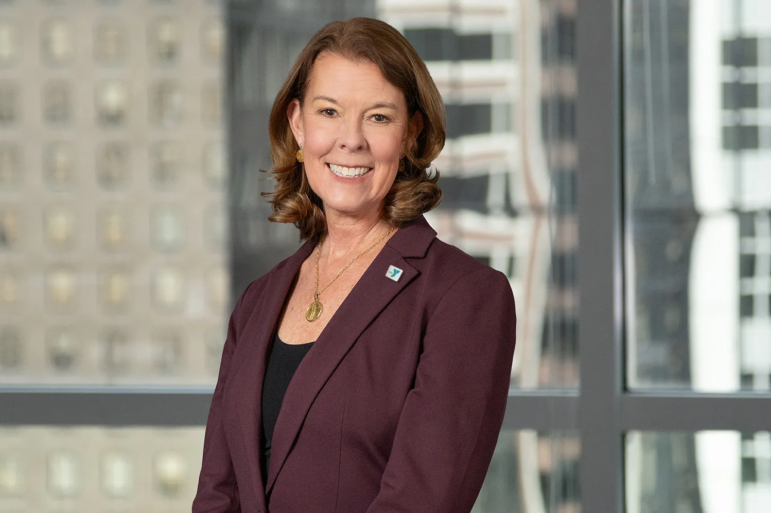 Photo of Suzanne McCormick - Y-USA President in a burgundy suit jackt with buildings in the background
