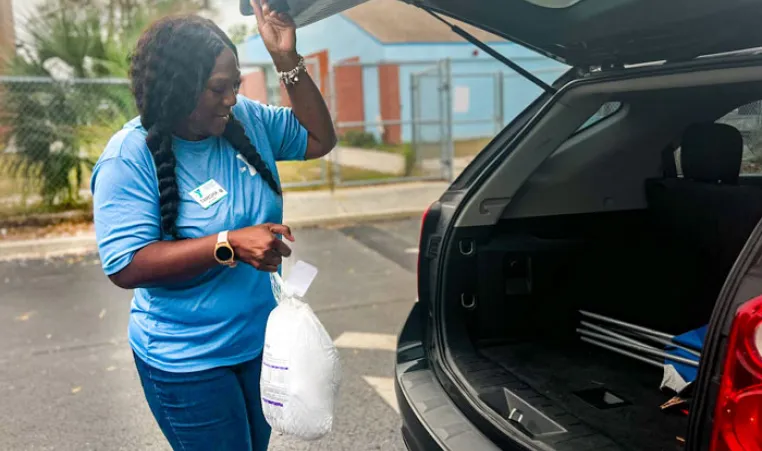 A YMCA volunteer loads a turkey into a trunk.