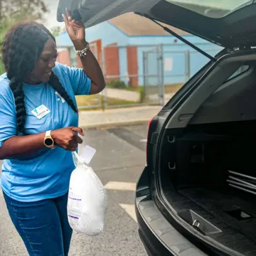 A YMCA volunteer loads a turkey into a trunk.