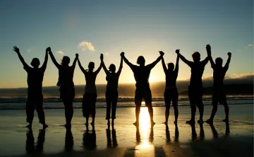 A group of people holding hands on beach as they face the sunset