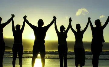 silhouette of people holding raised hands on beach at sunrise